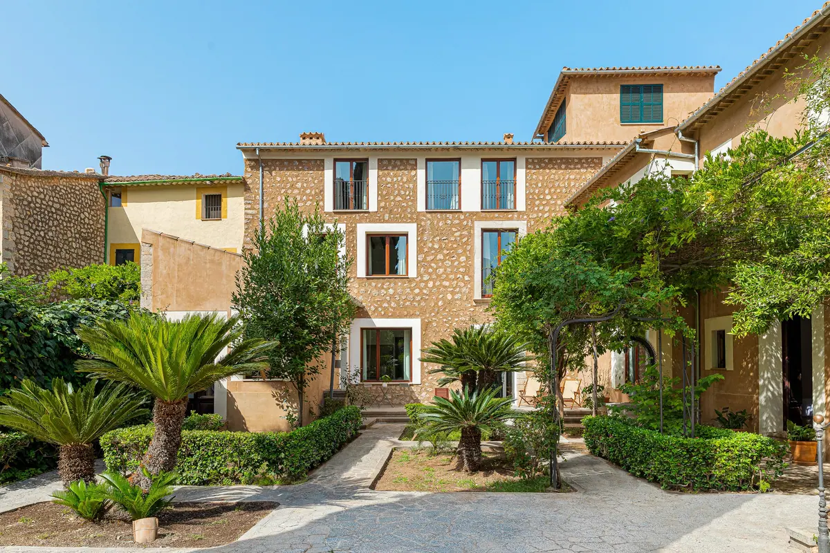 Stone façade of a building with a garden of palms and hedges