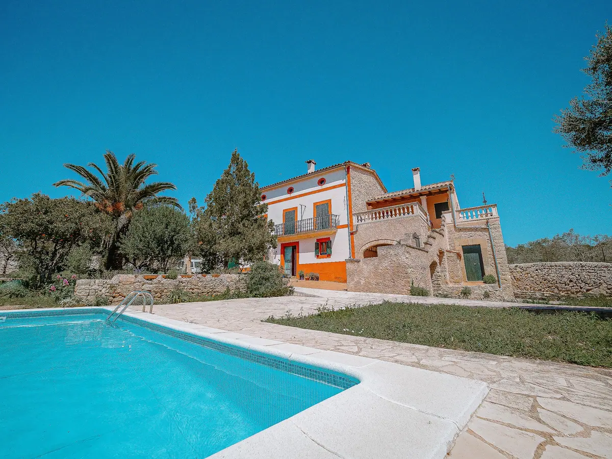 Stone country house with pool, lawn and palm tree under blue sky